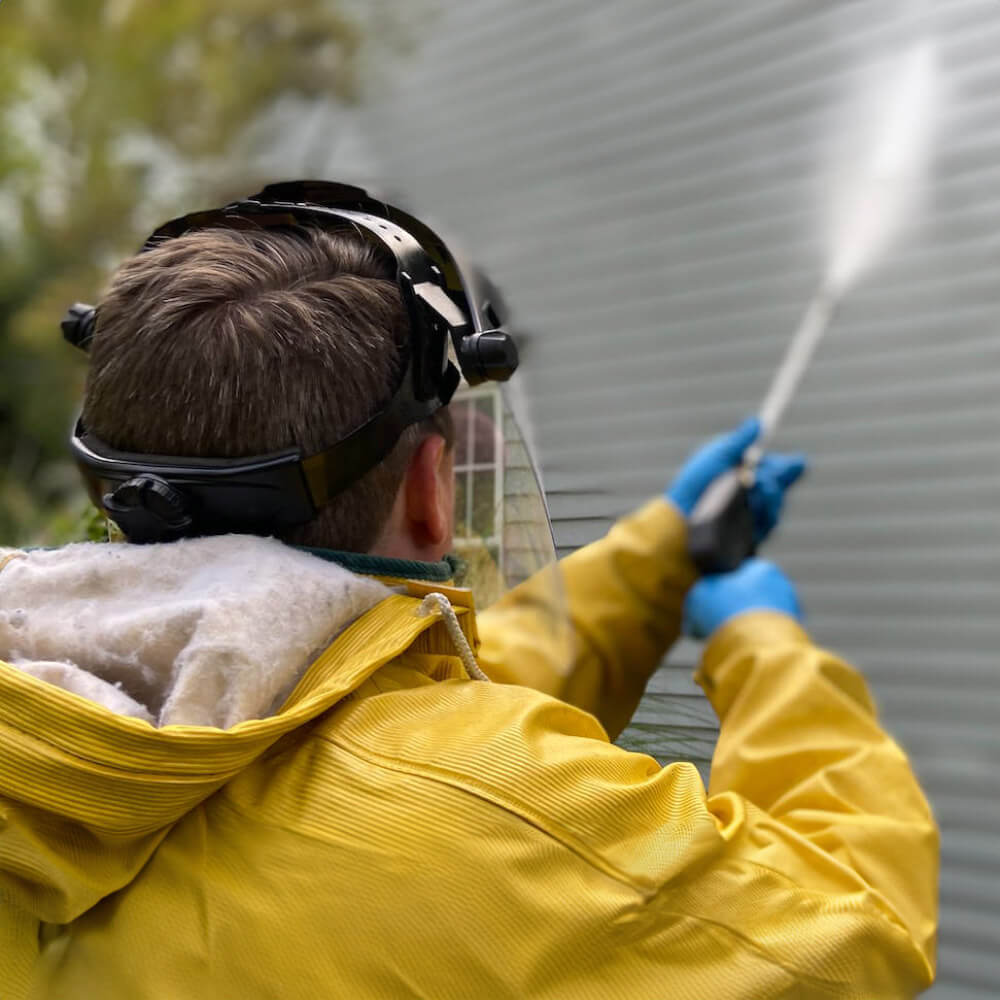 A man wearing a yellow rain jacket spraying a wall with a power washer.